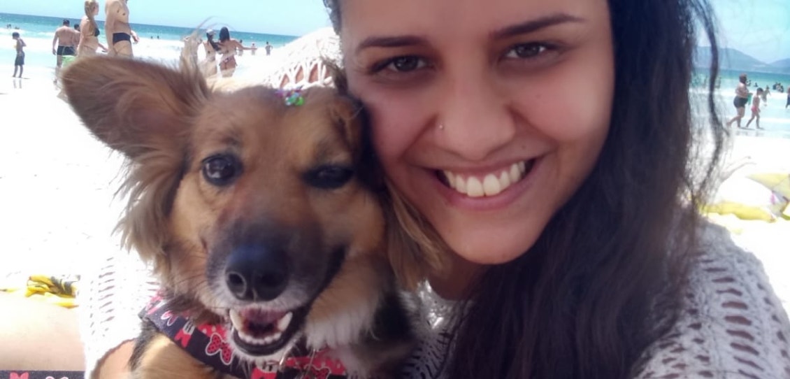 Mulher e cachorro abraçados com o mar e céu azul ao fundo 