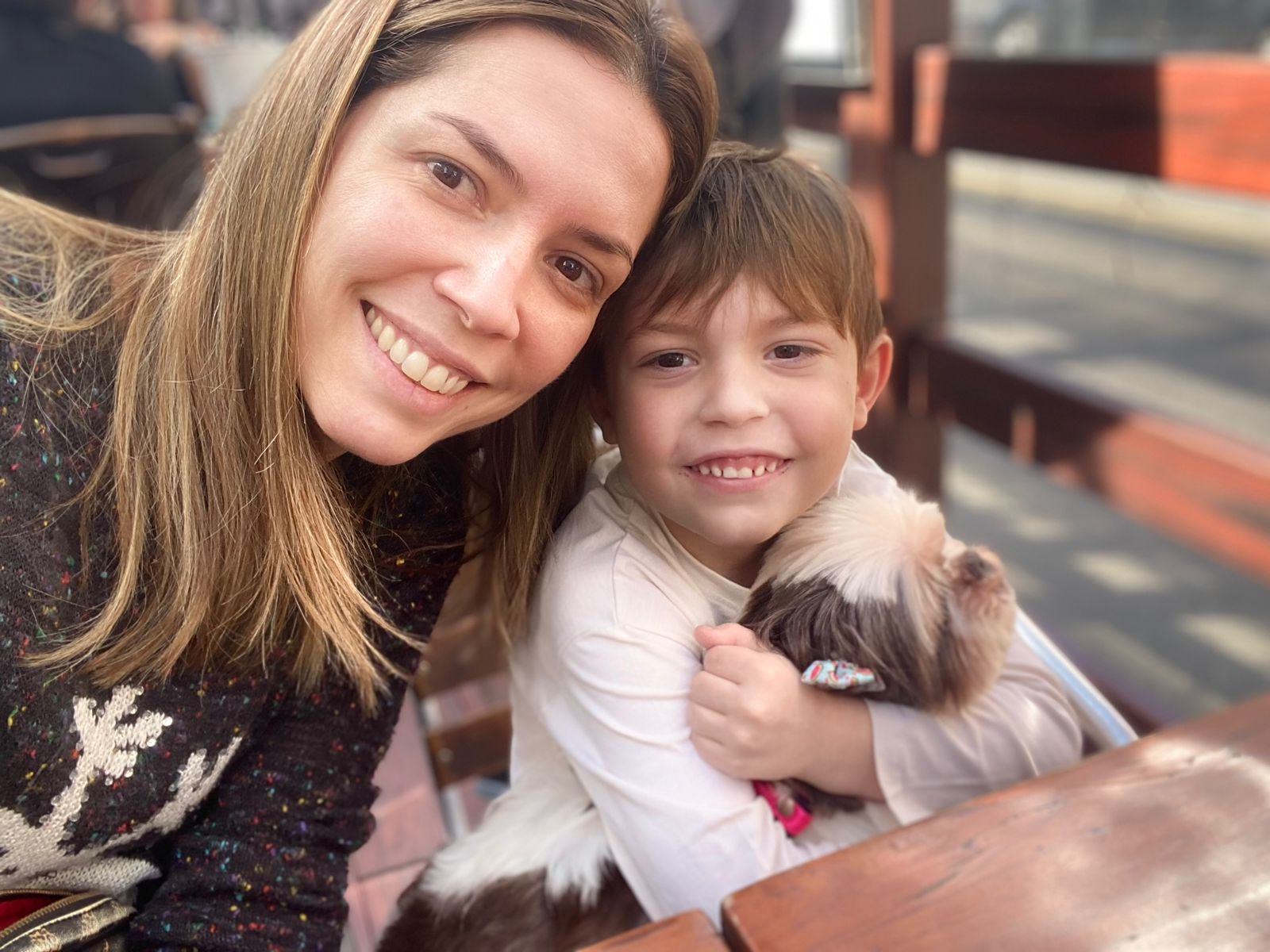 Selfie da Débora ao lado de seu filho que está segurando a Cupcake, uma shih-tzu cega. 