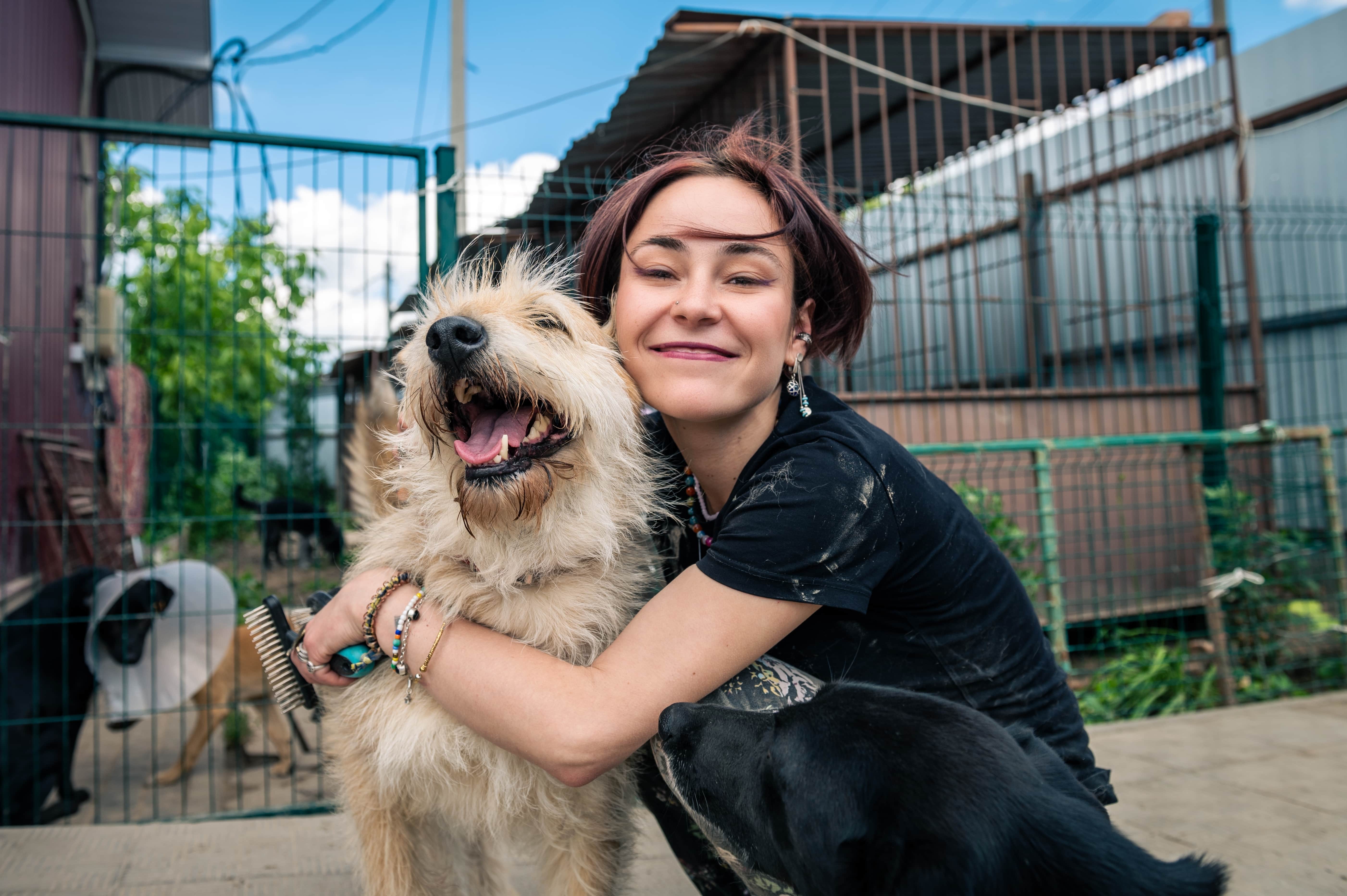 Mulher sorrindo, abraçando um cachorro em um abrigo